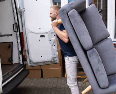 Möbellift Ludwigshafen: Helfer tragen ein graues Sofa aus einem Transporter